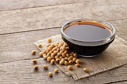 soy sauce in glass bowl with dry soybeans on wooden table