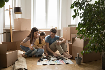 Happy engaged parents and little daughter girl choosing colors for new home interior, reviewing...