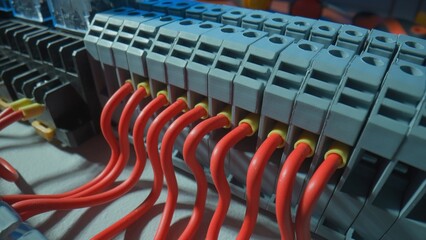 Gray plastic electrical panel with many red wires, yellow bushing ferrules screwed to the panel, electrical parts, automatic switches, breakers. Close up of a high voltage electrical switch.