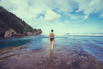Vacation on the seashore. Back view of young woman enjoying the view of the beautiful tropical natural rock pool.