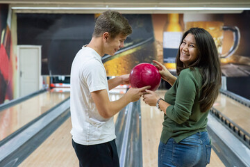 A guy and a beautiful and smiling girl bowling