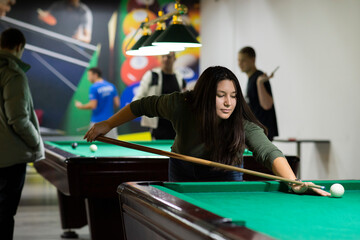 A young and beautiful woman with long hair is playing billiards in a club