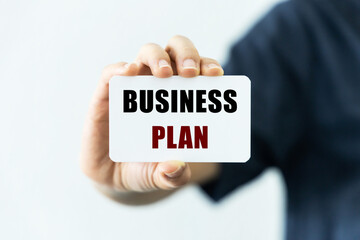 Business plan text on blank business card being held by a woman's hand with blurred background. Business concept about business plan.