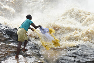 Indian fisherman throwing cast net in the river wave.