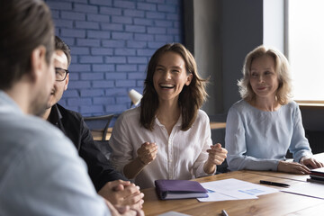 Cheerful young office employee girl meeting with colleagues at office conference table, sharing idea, smiling, laughing, having fun. Diverse coworkers brainstorming, discussing sales