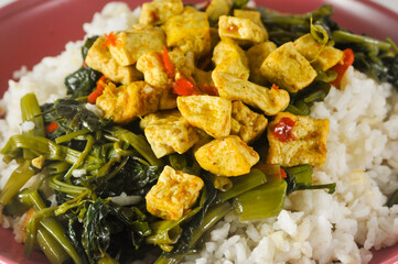 stir-fried water spinach with sliced tofu and white rice served on a red plastic plate with a napkin