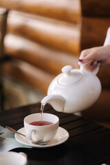 The waiter pours fruit tea into a white mug. Restaurant in a natural wooden style