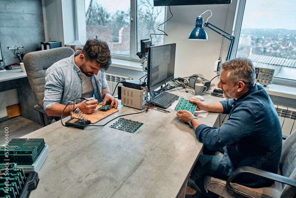 Wall mural two men sit at a table and work with microcircuits.concept of engineering, chip development and serv