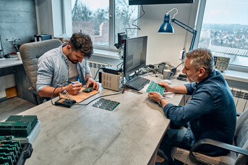 Two men sit at a table and work with microcircuits.Concept of engineering, chip development and service.