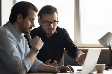 Focused engaged software developers discussing online application, looking at display, watching...