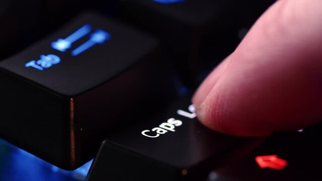 Human finger is clicking on the Caps Lock button on the computer keyboard, close up view. The finger presses Caps Lock on the keyboard key, macro shot. Loop footage.
