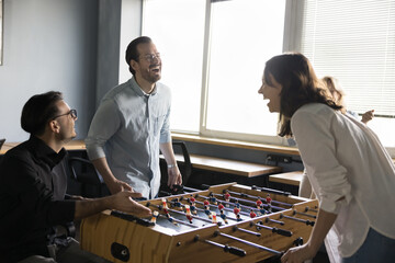 Joyful excited millennial couple of colleagues competing in table soccer on work break, laughing out loud at board game. Office friends playing tabletop football, having fun