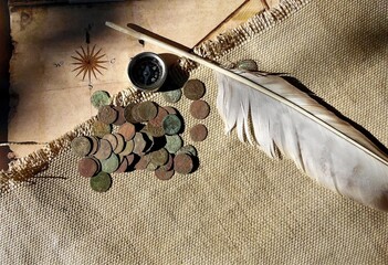 collage of antique 17th century copper coins, compass and feather on the background of an old map and burlap
