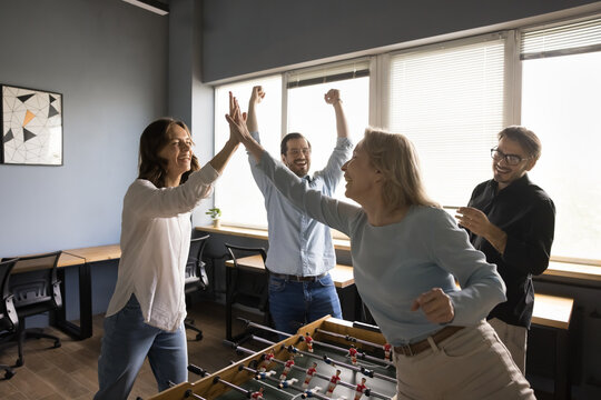 Happy excited two business colleagues women enjoying leisure, funny activity on work break, playing board game, competing in table soccer, winning, making high five gesture