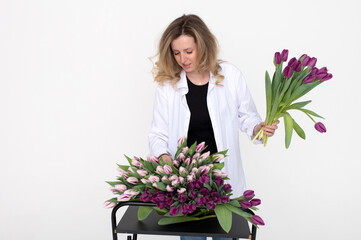 A cute girl takes a purple tulip from the table for a bouquet. Stands on a white background