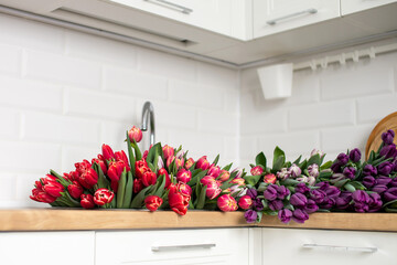A large number of tulips of different colors lies on the table in the kitchen. Flowers in the sink