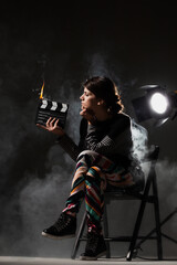 Female movie director on set with smoke background. Girl holding clapperboard on fire.