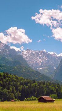 Idyllic mountain scenery, pasture, two small houses, evergreen forest and high rocky hills, timelapse, vertical short video