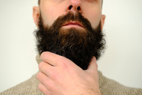 close-up of part of male face, young bearded man, guy with 30 years strokes his thick beard with his hand, concept of mustache and beard stubble care products, hairline hygiene on lower part of face