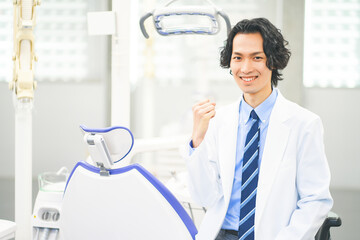 歯科治療ユニットの前でガッツポーズをする若い男性歯科医師