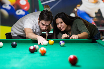 A guy and a young and beautiful woman are playing billiards in a club
