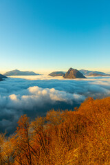 Mountain Peak San Salvatore Above Cloudscape with a Autumn Tree and Sunlight with Clear Sky in Lugano, Ticino in Switzerland.
