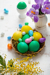 Fototapeta na wymiar Easter holiday still life with green and yellow eggs and flowers on light surface