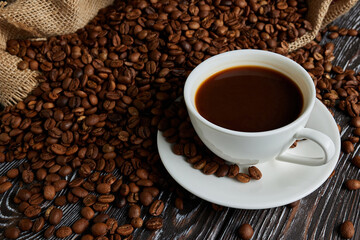 Cup of hot espresso coffee and coffee beans on dark black wooden background