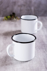 Two white empty metal mugs on a gray background in a vertical view