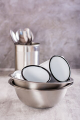 A set of metal utensils from bowls, enameled mugs and spoons on a vertical gray background