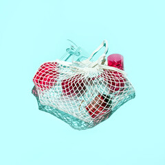 Fototapeta premium Various drinking glasses in a mash grocery bag, creative party concept, pastel blue background. 