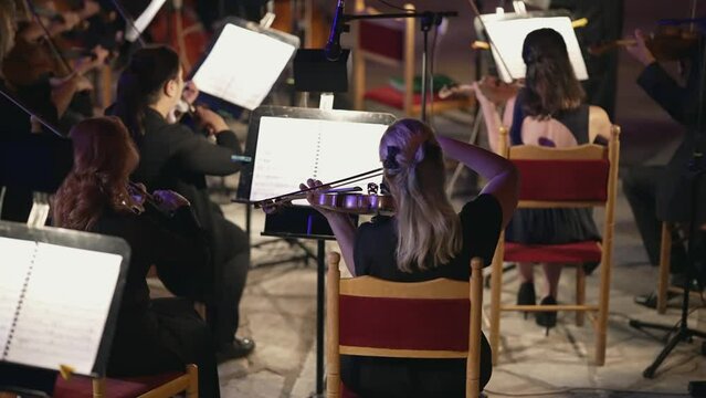 Chamber Music violin section players orchestra performing public no ticketing clasic music event on city square at night, slow motion cinematic shot