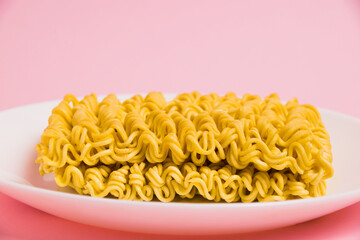 Instant noodles in a white plate on a pink background. Fast food in the modern world.