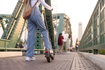 Portrait of young beautiful woman with an electric scooter  over bridge in modern city  background