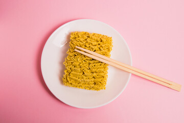 Flatlay, instant noodles in a white plate and chopsticks on a pink background