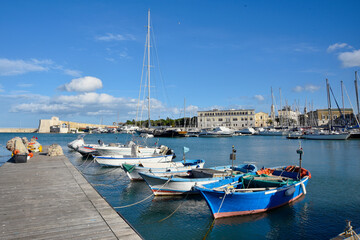 Fototapeta na wymiar Fishing boats docked at the piers in Trani, Italy. View of historical buildings, turquoise water and clear sky