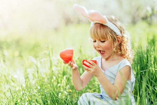 Easter egg hunt. Girl child Wearing Bunny Ears Running To Pick Up Egg In Garden. Easter tradition. Baby with basket full of colorful eggs.