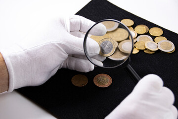 An expert or collector examines coins through a magnifying glass, collection business concept