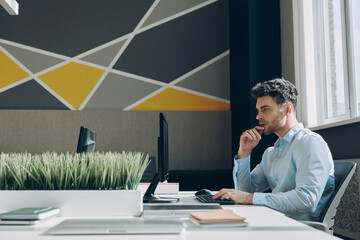 Concentrated young businessman using computer while sitting at his working place in office