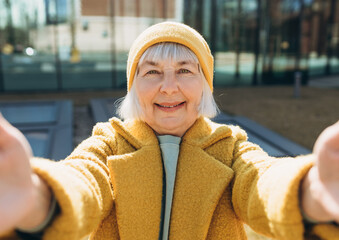 Beautiful senior blonde woman taking selfie on sity street. Looking at camera and smile. Travel and...