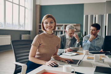 Three business people working together in office while young woman looking at camera and smiling