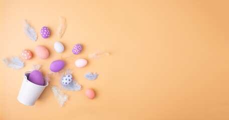 Colorful Easter eggs with feathers in decorative bucket on beige background, flat lay. Space for text
