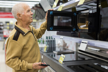 elderly grayhaired man pensioner looking microwave oven at counter in showroom of electrical appliance hypermarket department
