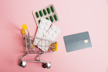 Bank card, credit card, pills, shopping cart on pink background with copy space, flat lay. Concept...