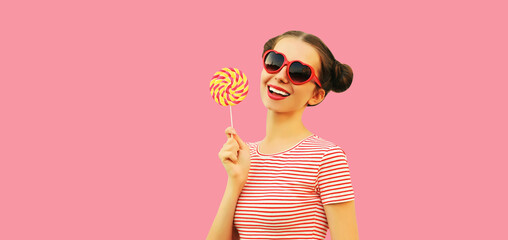 Summer portrait of happy smiling young woman with colorful lollipop wearing red heart shaped sunglasses on pink background