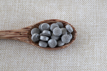 Round brown tablets with spots on a beige background in a wooden spoon. Iron supplements. Health medication. Close-up