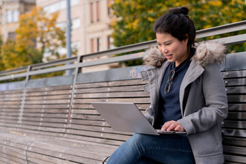 cheerful asian female digital nomad meeting online working with global partners around the world while travel, asia woman working online via laptop vpn on wooden bench in public city park