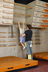 Fototapeta premium Kid girl at climbing wall with male instructor in climbing center
