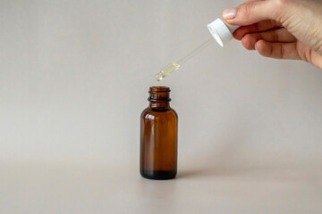 The Young Woman's hand holds a bottle with a dropper, with an oil or serum for facial and body...