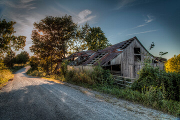 Barn on a Gravel Road. Evening sunlight blast through the leaves of a tree in the late hours of the...